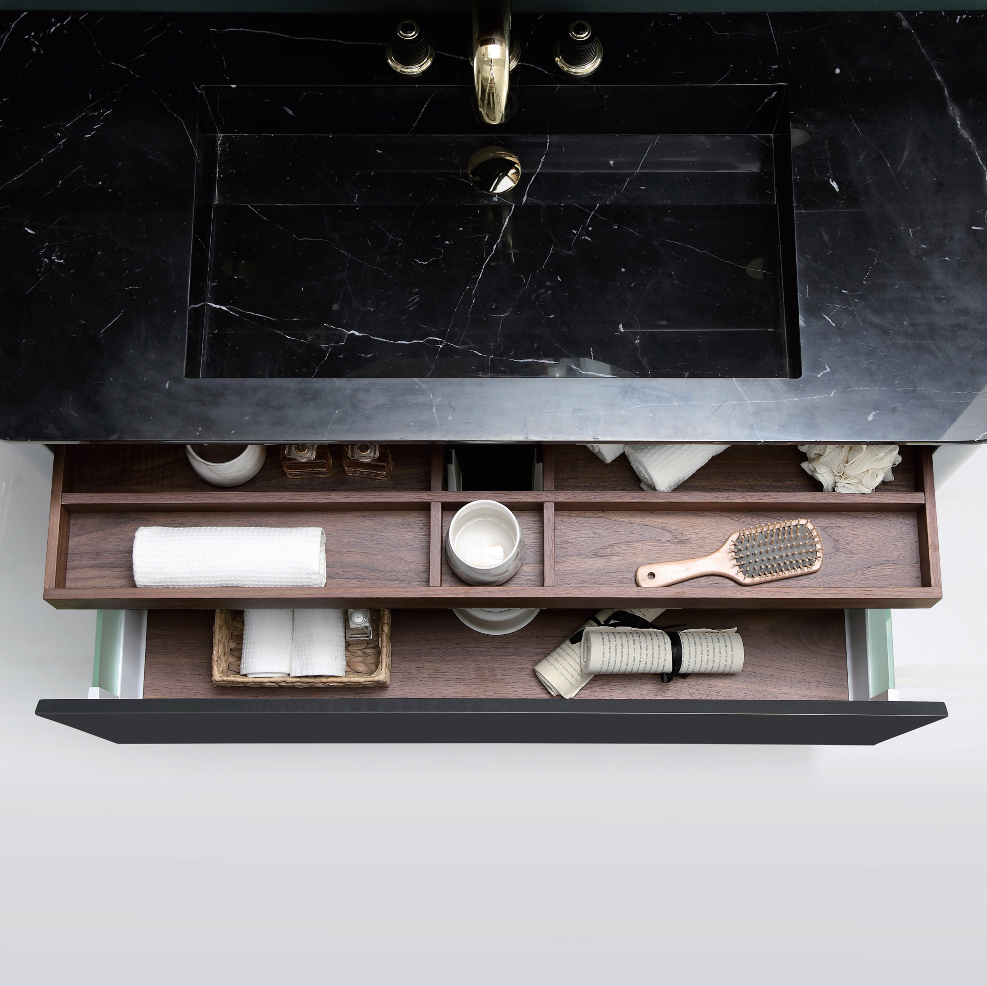 Utdragne skuffer i valnøtt sett ovenfra på Eterra baderomsmøbel fra Brandt Bad. Den øvereste skuffen er inndelt i flere mindre rom. Den større skuffen har glassider. Benkeplate med nedsenket servant i sort marmor.