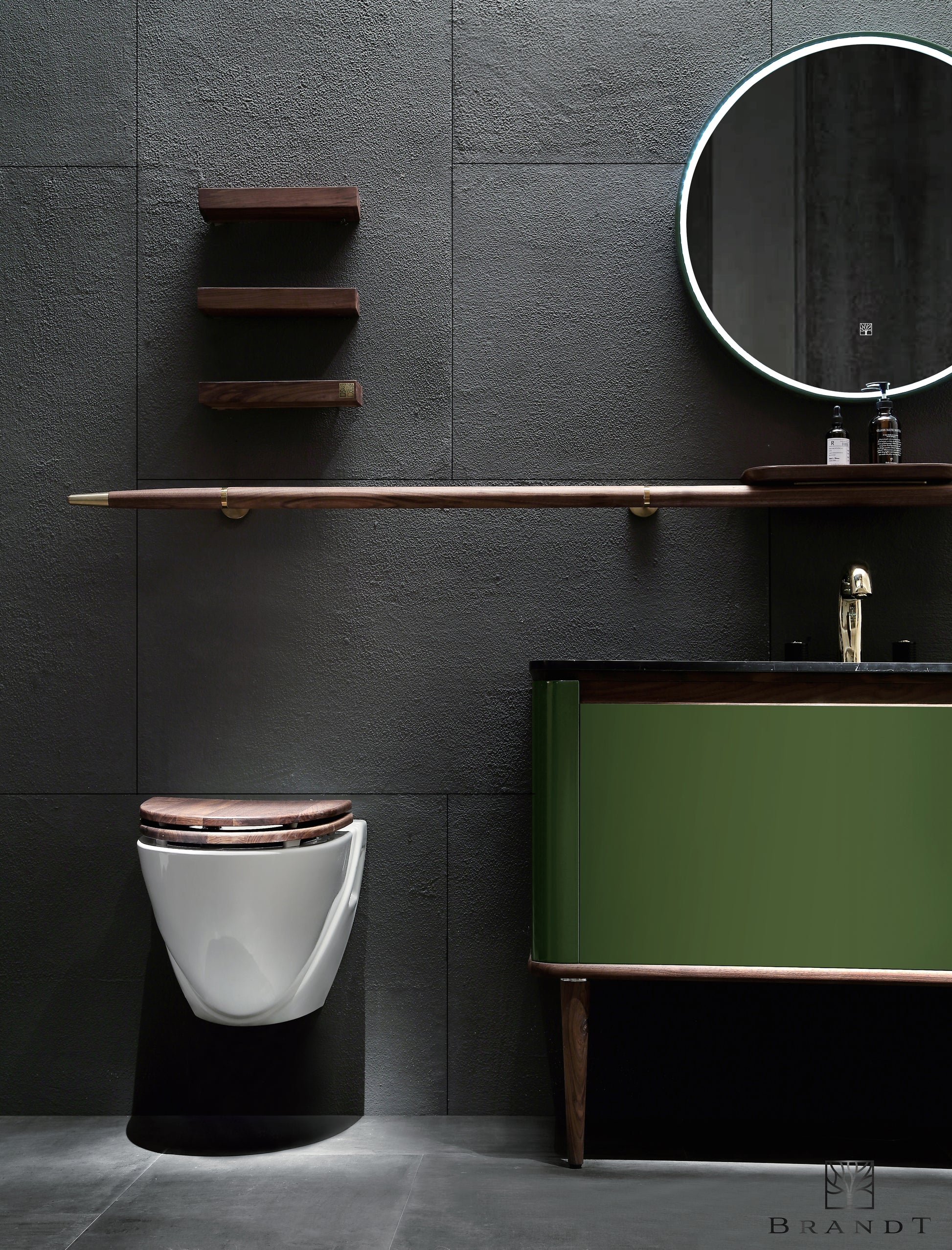 Nærbilde av Eterra baderomsinnredning fra Brandt Bad. Unikt og vakkert møbel med grønn speilblank lakkmaling og detaljer i valnøtt og messing. Servant i sort marmor. Tilbehør er en lang rund håndklestang i valnøtt med en påmontert liten hylle. Rundt speil med integrert LED belysning, og tre vakre vegghyller i valnøtt.