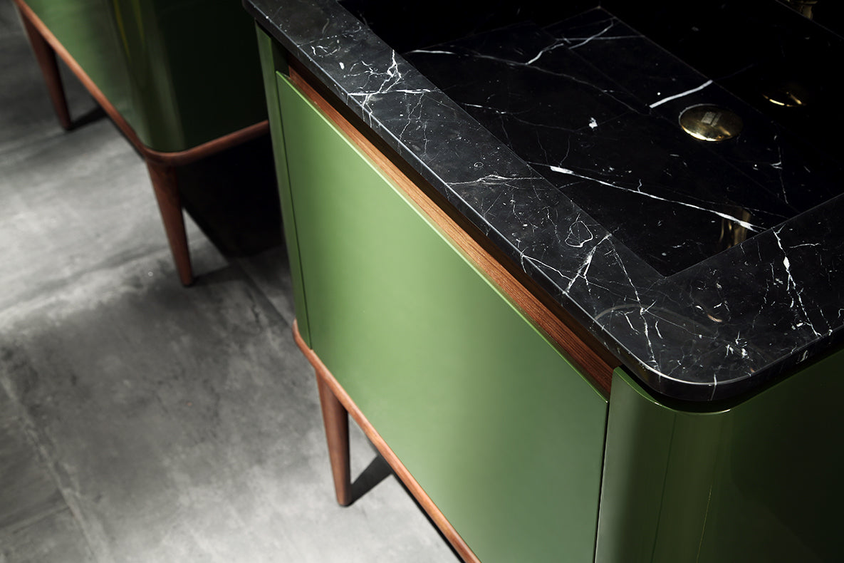 Närbilde av Eterra baderomsmøbel fra Brandt Bad sett på skrått ovenfra. Benkeplate med nedsenket servant i Spansk Nero Marquis marmor. Speilblanke fronter i grønn pianolakk med avrundede hjørner, og detaljer i valnøtt.