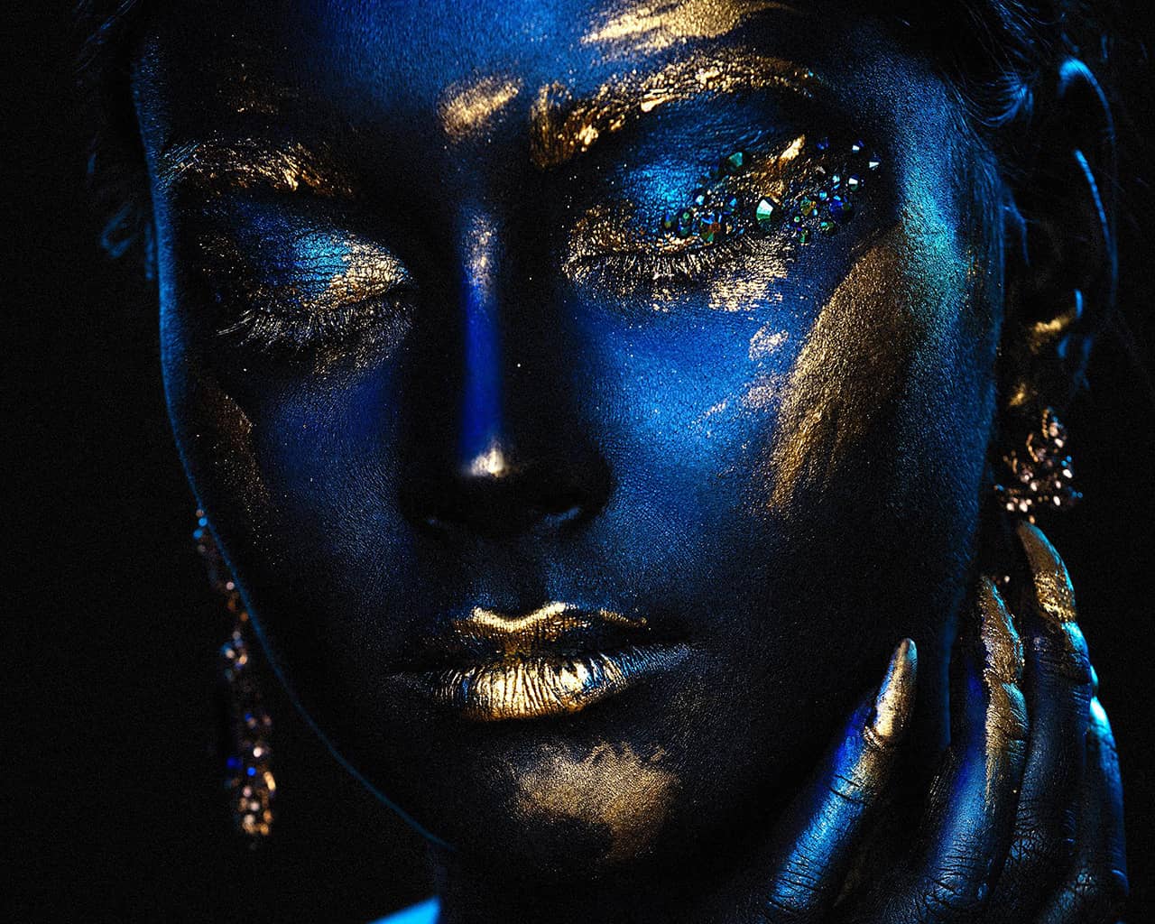 Nærbilde av blåmalt ansikt med lukkede øyne og gulldetaljer.