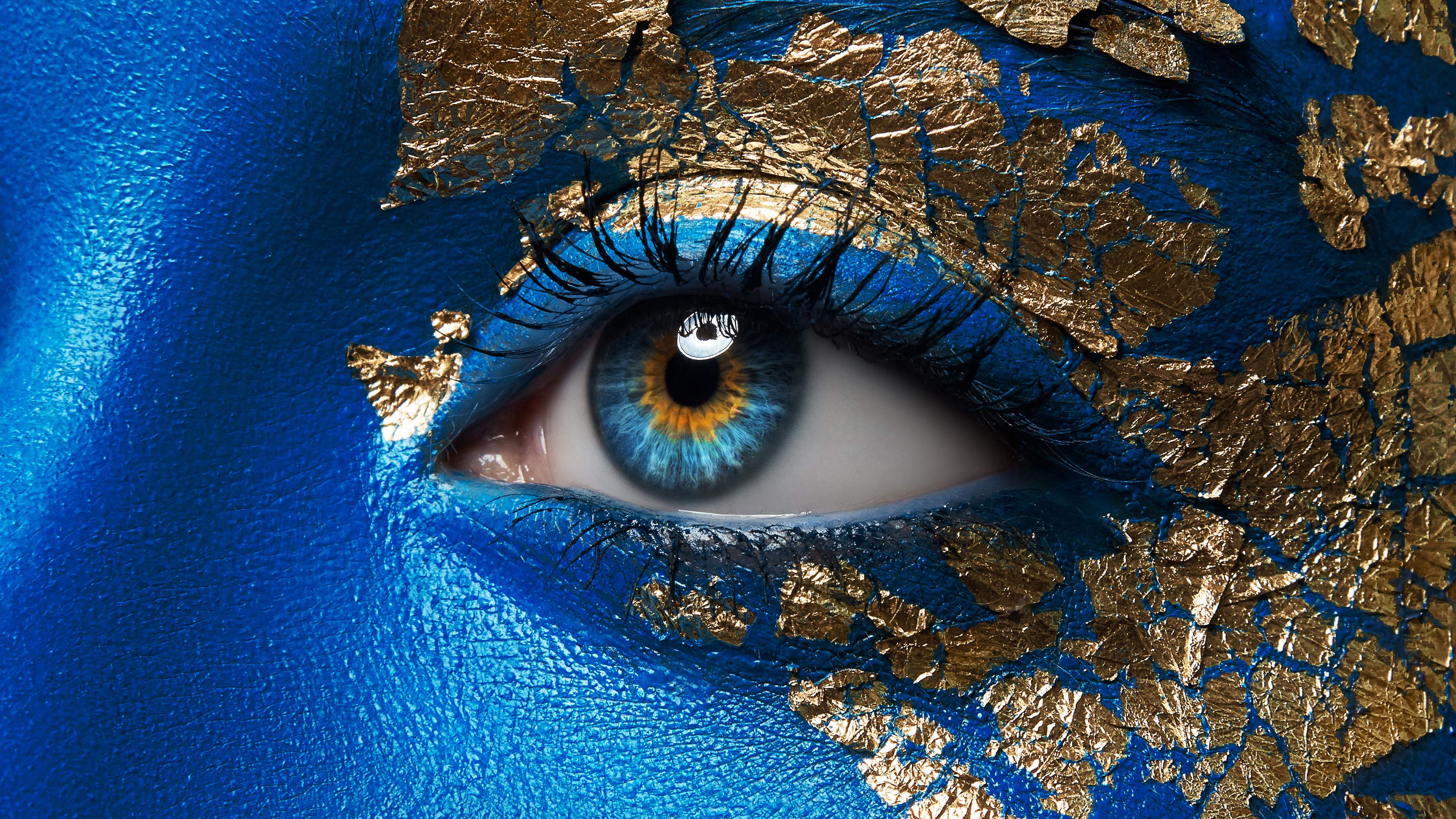 Nærbilde av åpent øye på blåmalt ansikt med gulldetaljer.